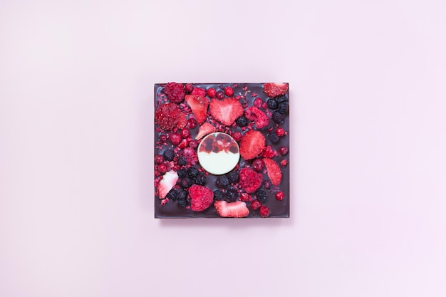 Kwadrat ciemnej czekolady z jagodami na różowym tle nalewa czekoladę Widok z góry