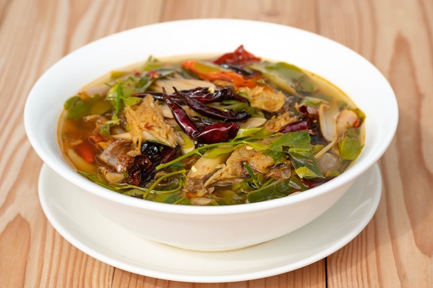 Kwaśno-pikantna wędzona sucha zupa rybna w białym ceramicznym talerzu na drewnianym stole. Tom Klong W języku tajskim. Tajskie jedzenie.