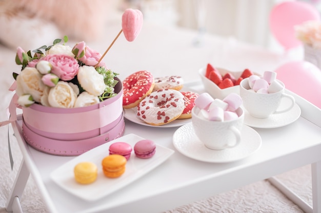 Kwiaty i słodycze na białym stole i balony na białym łóżku. Prezent na Dzień Matki