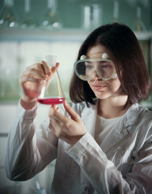 Laboratorium chemiczne młoda kobieta w okularach roboczych patrząc na kolbę