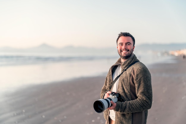 Łaciński fotograf trzymający profesjonalny aparat na plaży i uśmiechnięty portretx9