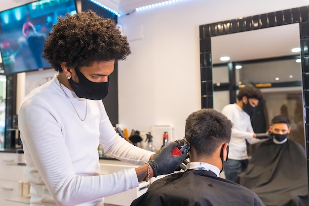 Łaciński fryzjer w masce i rękawiczkach obcinający klientowi włosy brzytwą