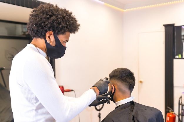 Łaciński fryzjer w masce i rękawiczkach obcinający klientowi włosy brzytwą