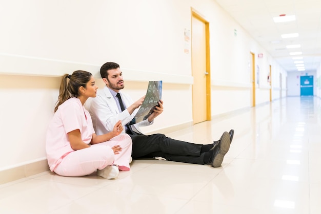 Zdjęcie Łaciński lekarz i pielęgniarka omawiają raport rentgenowski, siedząc pod ścianą w korytarzu w szpitalu