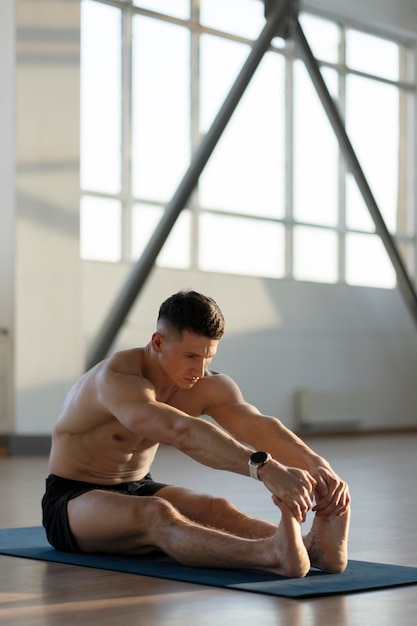Łaciński lekkoatleta rozciągający się przygotowujący do treningu w siłowni Atrakcyjny mężczyzna z gołym torsem uprawiający sport