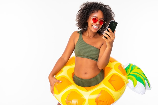Ładna afrykańska kobieta w swimsuit stoi z dużym kolorowym gumowym pierścionkiem i komunikuje się z przyjaciółmi lub rodziną z jej telefonem i uśmiecha się odosobnionego