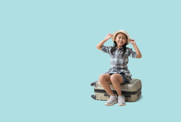 Ładna azjatycka dziewczynka siedzi na walizce przygoda podróż wakacje podróż marzenie koncepcja Uśmiechnięta śliczna dziewczynka odizolowana na niebieskim tle ze ścieżkami przycinającymi do prac projektowych pusta wolna przestrzeń