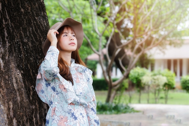 Ładna azjatykcia dziewczyna w rocznik sukni opiera przeciw na relaksować i drzewie.