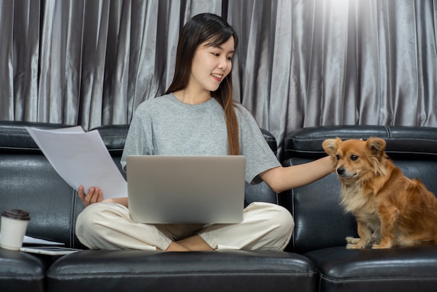 Ładna azjatykcia kobieta pracuje zdalnie z domu używać laptopu obsiadanie na kanapie lub kanapie