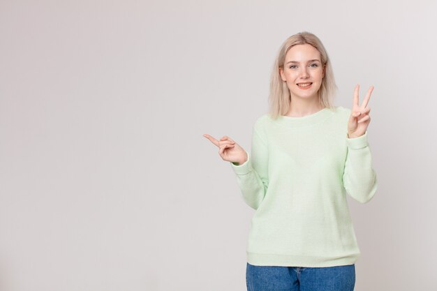 Ładna blond kobieta uśmiechająca się i wyglądająca przyjaźnie, pokazująca numer dwa