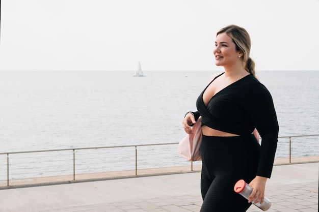 Ładna blondynka plus size spaceruje ze sportową odzieżą i butelką wody po ćwiczeniach