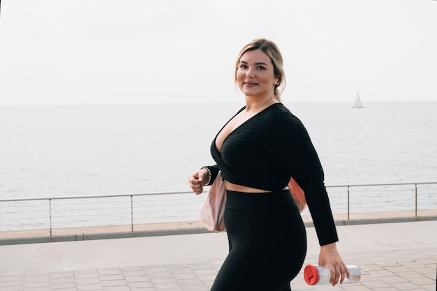 Ładna blondynka plus size spaceruje ze sportową odzieżą i butelką wody po ćwiczeniach