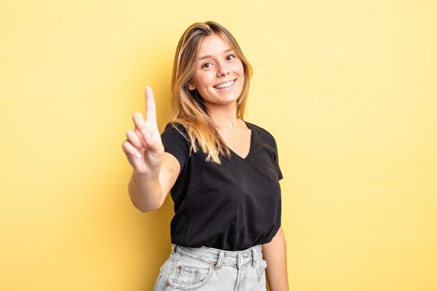 Ładna blondynka uśmiecha się dumnie i pewnie robi triumfalną pozę numer jeden, czując się jak lider