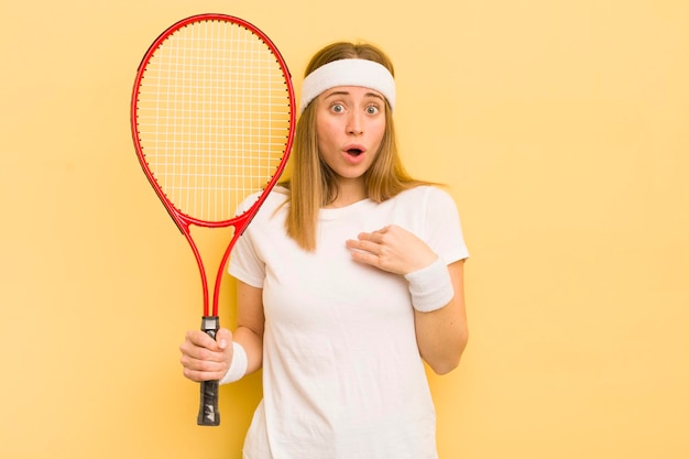 Ładna blondynka wygląda na zszokowaną i zaskoczoną z szeroko otwartymi ustami, wskazując na koncepcję tenisa własnego