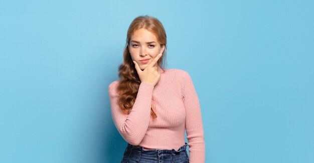 Ładna blondynka wyglądająca poważnie, zamyślona i nieufna, z jedną ręką skrzyżowaną i ręką na brodzie, opcje ważenia