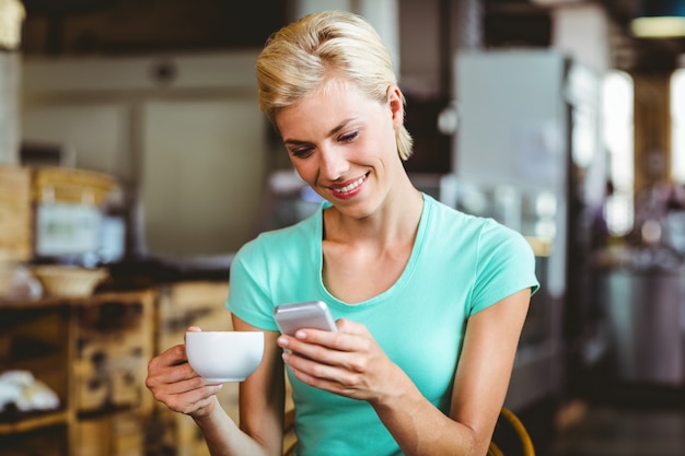 Ładna blondynki kobieta używa jej smartphone z filiżanką kawy