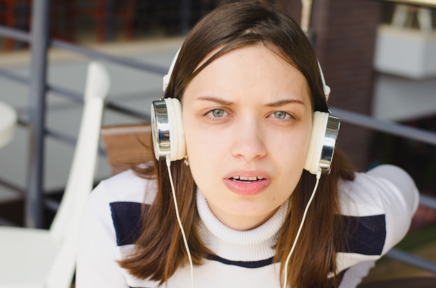 Ładna brunetka dziewczyna słucha muzyki w kawiarni w białych słuchawkach