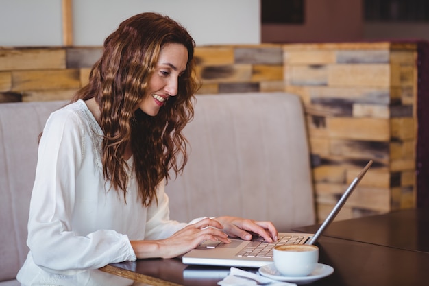 Ładna brunetka ma kawowego używa laptop