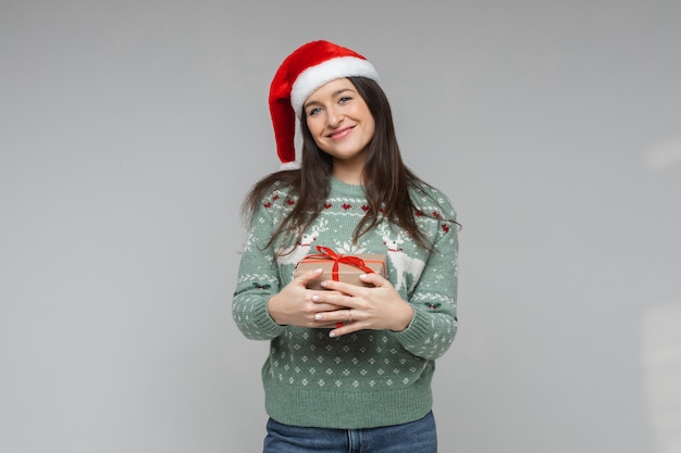 Ładna brunetka w santa hat obejmując prezent.