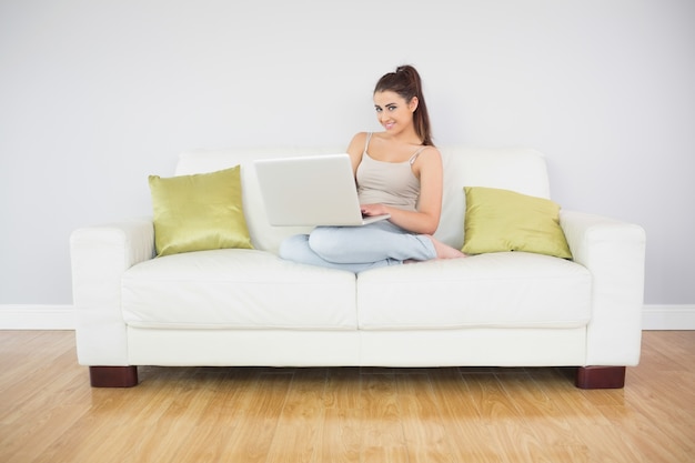 Ładna brunetki kobieta używa jej laptop na kanapie