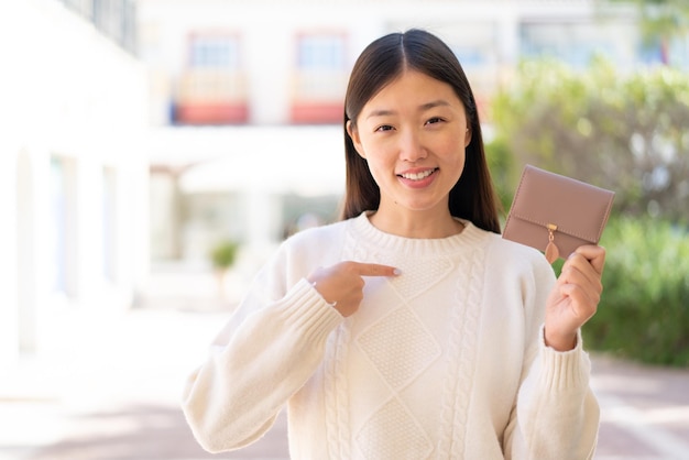 Zdjęcie Ładna chinka trzyma portfel na zewnątrz z wyrazem twarzy zaskoczenia