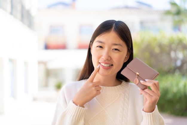 Ładna chińska kobieta trzyma portfel z szczęśliwym wyrazem twarzy na zewnątrz
