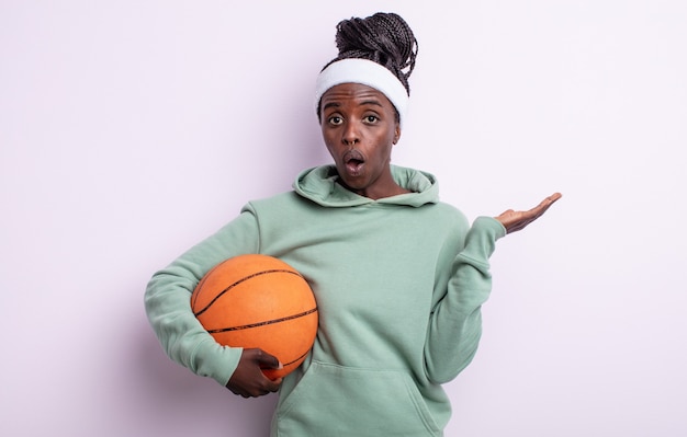 Ładna czarna kobieta wyglądająca na zaskoczoną i zszokowaną, z opuszczoną szczęką trzymająca przedmiot. koncepcja koszykówki