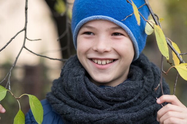 Ładna Dziecko Chłopiec Jest Ubranym Ciepłego Zimy Odzieżowego Mienia Gałąź Z Zielonymi Liśćmi W Zimnej Pogodzie Outdoors.