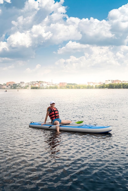 Ładna dziewczyna nosi kamizelkę ratunkową odpoczywa i opala się na desce surfingowej po treningu