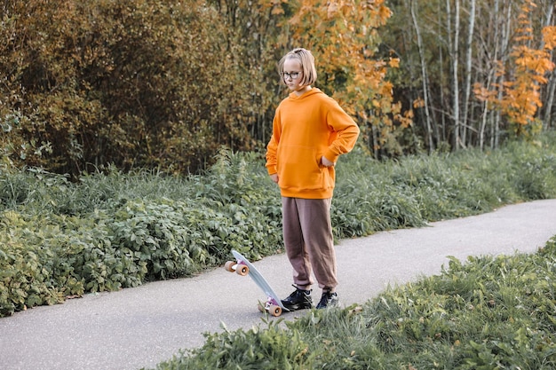 Ładna dziewczyna uczy się jeździć na deskorolce na zewnątrz w piękny jesienny dzień. Zajęcia dla dzieci i koncepcja aktywnego stylu życia.