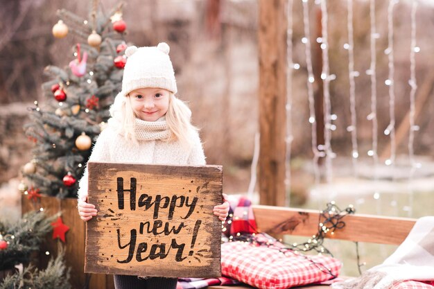 Ładna dziewczynka trzyma drewniany stół ze znakiem szczęśliwego nowego roku na zewnątrz