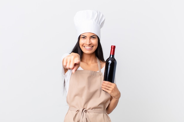 Ładna hiszpańska kobieta szefa kuchni, wskazując na kamerę, która cię wybiera i trzyma butelkę wina