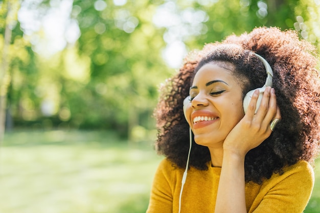 Ładna kobieta afro słucha muzyki ze słuchawkami tańczy w ogrodzie. Selektywne skupienie.