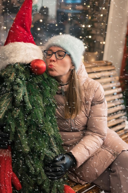 Ładna kobieta całuje drzewo zdobione manekinem boże narodzenie święta nowy rok lub koncepcja bożego narodzenia