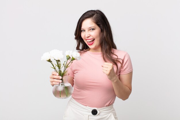 Ładna kobieta czuje się zszokowana, śmieje się i świętuje sukces i trzyma ozdobną doniczkę z kwiatami