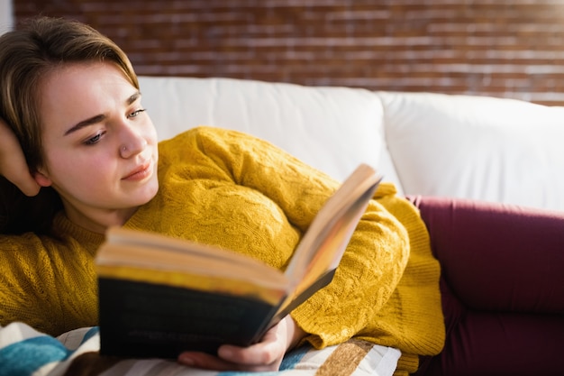 Ładna kobieta czyta książkę leżąc na kanapie w salonie