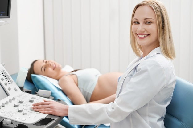 Ładna kobieta, doktorski pozować podczas gdy robić ultrasonografii.
