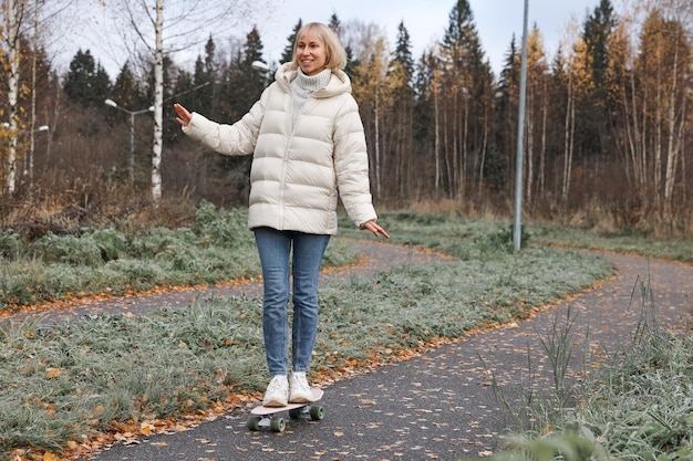 Zdjęcie Ładna kobieta jeździ na deskorolce w jesiennym parku, uczy się jeździć na deskorolce, spędzając weekend na świeżym powietrzu na świeżym powietrzu. koncepcja zdrowego sportu.