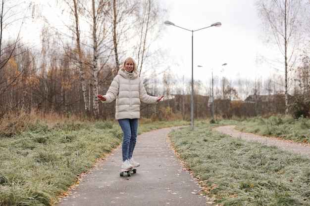 Ładna kobieta jeździ na deskorolce w jesiennym parku, uczy się jeździć na deskorolce, spędzając weekend na świeżym powietrzu na świeżym powietrzu. Koncepcja zdrowego sportu.