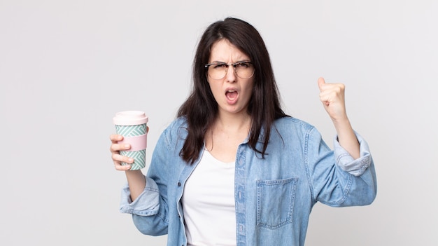 Ładna kobieta krzyczy agresywnie z gniewnym wyrazem twarzy i trzyma kawę na wynos