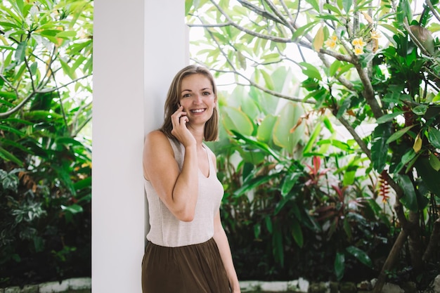 Ładna kobieta oparta na kolumnie i rozmawiająca przez telefon na podwórku willi
