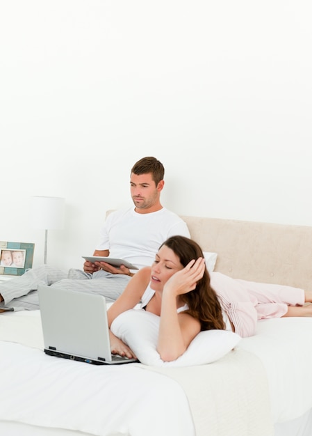 Ładna kobieta pracuje na jej laptopie, podczas gdy jej mąż czyta książkę