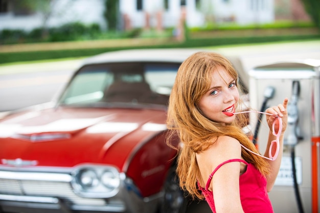 Ładna kobieta tankuje samochód Stacja benzynowa Elegancka dama na tle czerwonego samochodu retro