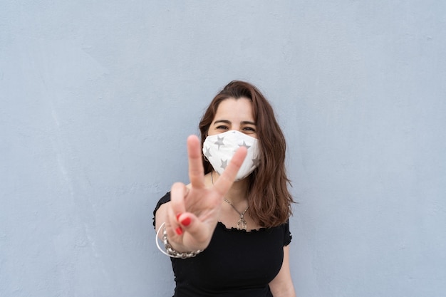Ładna kobieta ubrana w maskę i robiąca ręką znak pokoju