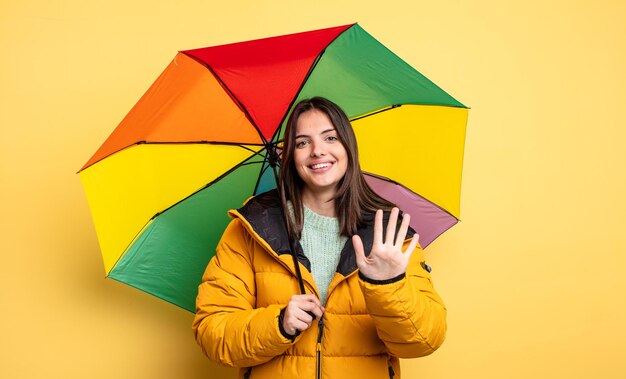 Ładna kobieta uśmiechnięta i patrząca przyjaźnie, pokazując numer pięć. koncepcja zima i parasol