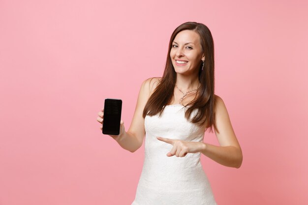 Ładna kobieta w białej sukni wskazując palcem wskazującym na telefonie komórkowym z pustym czarnym pustym ekranem