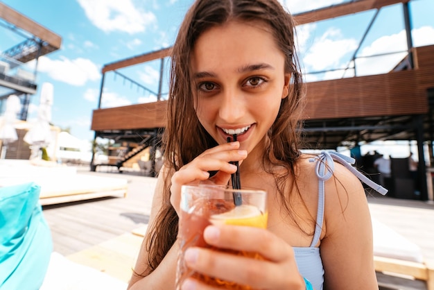 Ładna kobieta w bikini pije koktajl na imprezie przy basenie