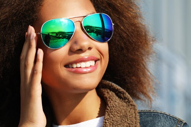 Ładna kobieta w okularach przeciwsłonecznych z idealnymi zębami i ciemną czystą skórą, która odpoczywa na świeżym powietrzu