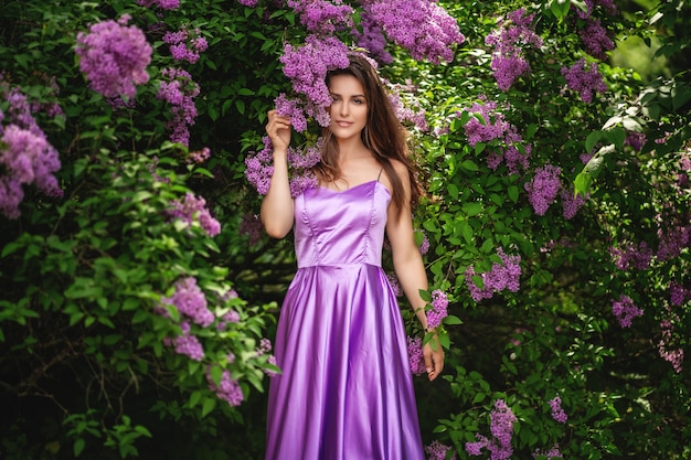 Ładna kobieta w purpury sukni pozuje blisko lilych drzew