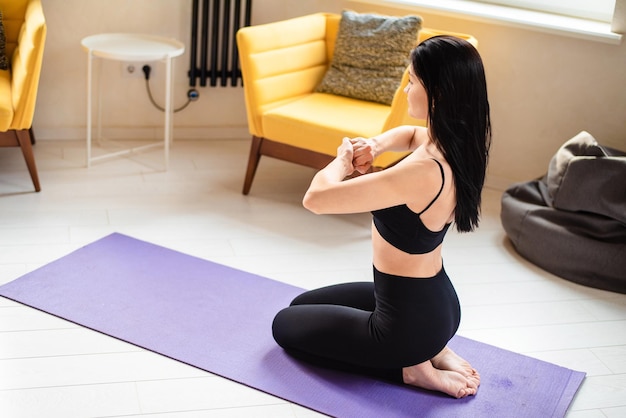 Ładna kobieta w sportowym ubraniu medytująca na macie do jogi z zamkniętymi oczami Zdrowa młoda brunetka ćwiczy jogę, pozostając sama w domu